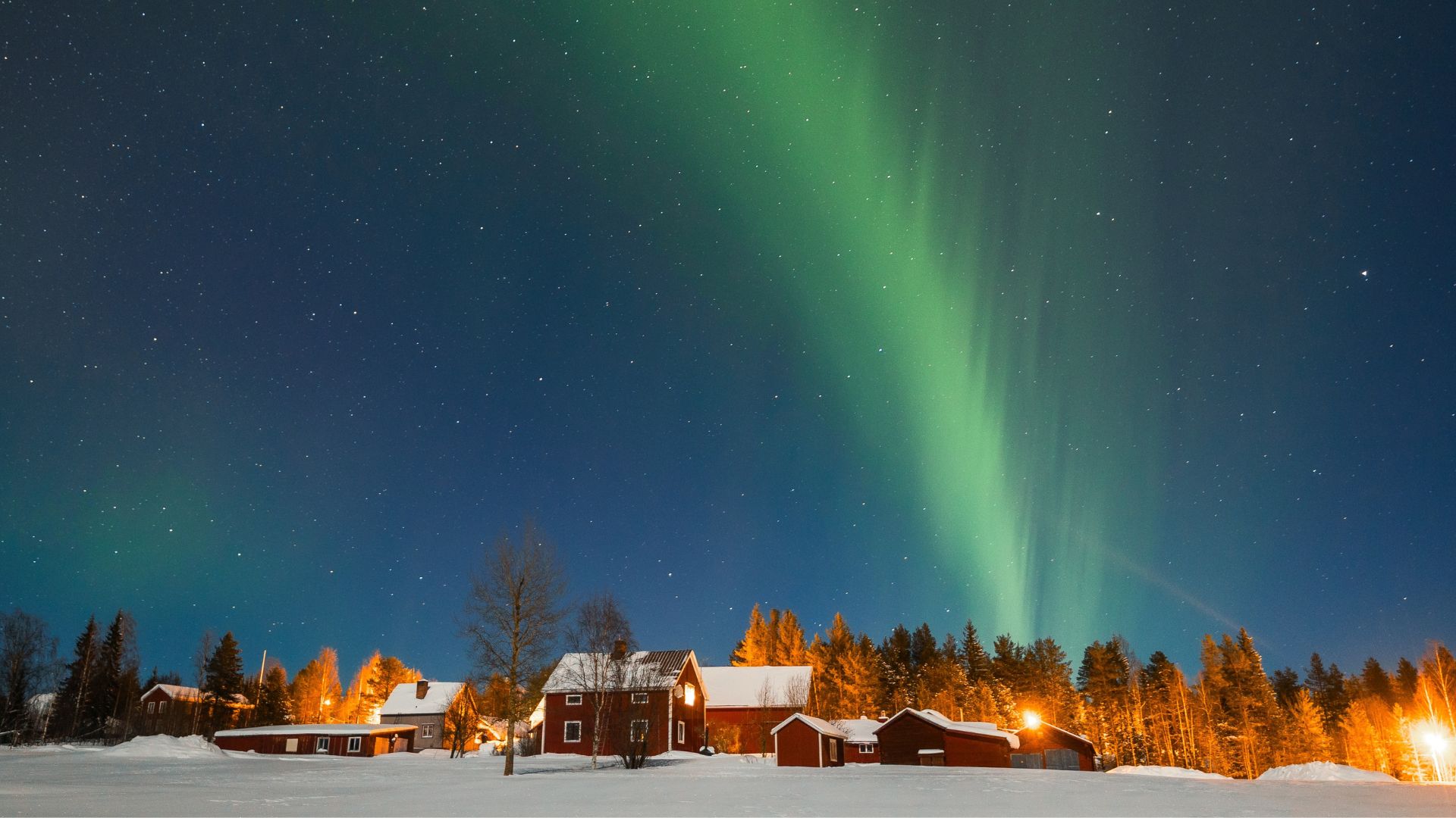 Green aurora borealis lights up the night sky above red wooden houses and snow-covered ground, creating a magical travel getaway with trees, bush, and twinkling stars in the background.