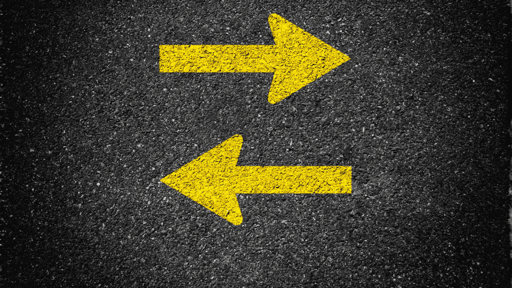 Two bold yellow arrows painted on asphalt, one pointing right and the other left, indicate two-way traffic or opposite directions—common near SDA parking lots for clear guidance.