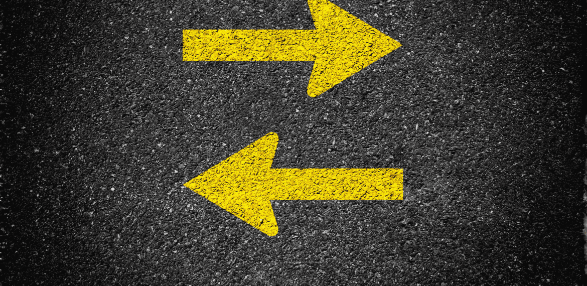 Two bold yellow arrows painted on asphalt, one pointing right and the other left, indicate two-way traffic or opposite directions—common near SDA parking lots for clear guidance.