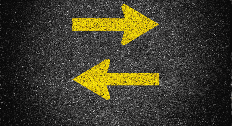 Two bold yellow arrows painted on asphalt, one pointing right and the other left, indicate two-way traffic or opposite directions—common near SDA parking lots for clear guidance.