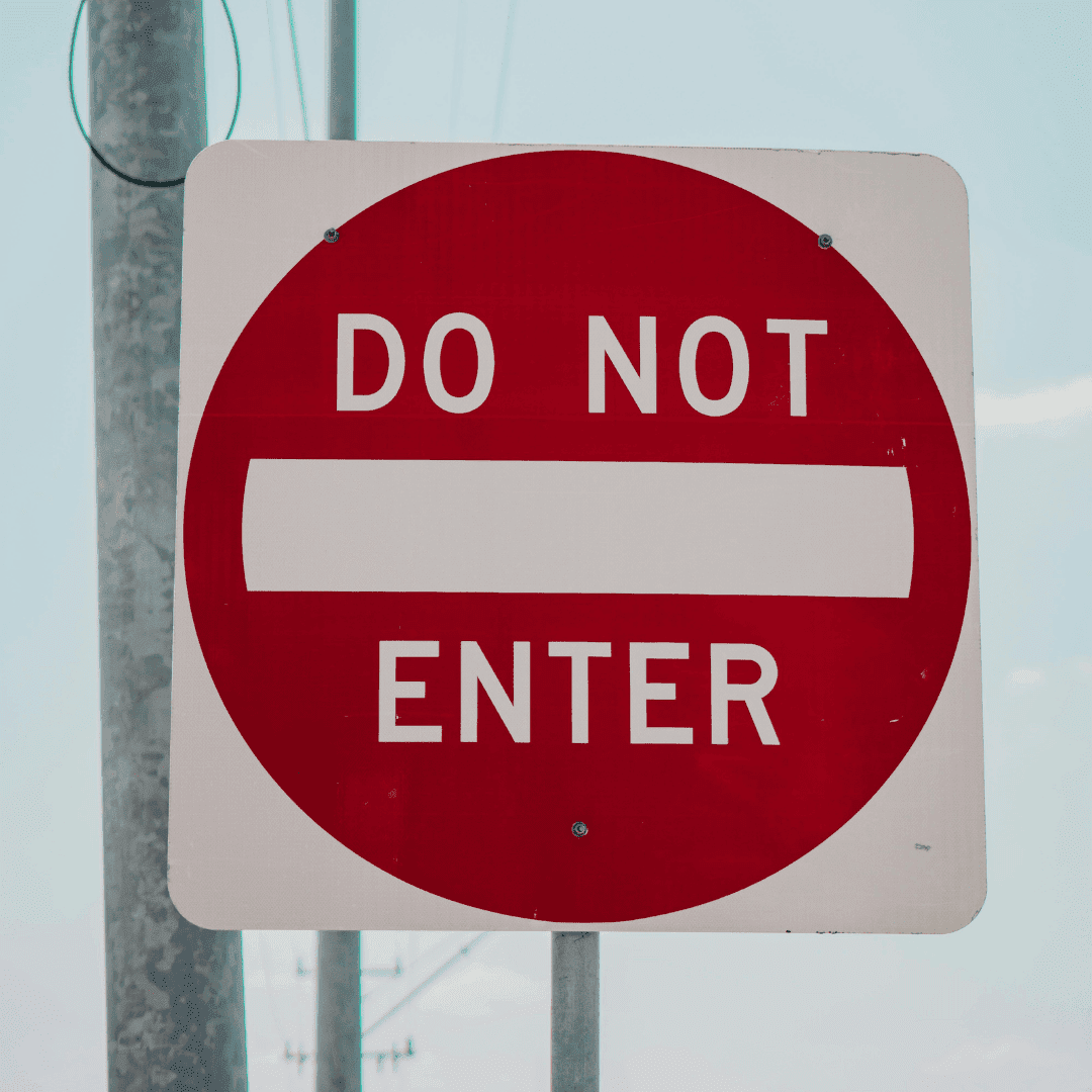 A red and white Do Not Enter road sign is mounted on a pole, signaling vehicles that entry is not allowed in this SDA zone. The background shows a clear sky and part of another pole.