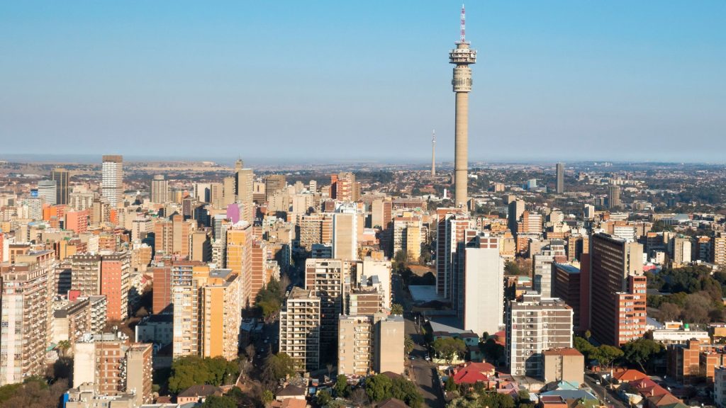 Aerial view of a cityscape with many tall buildings and a prominent telecommunications tower in the center, under a clear blue sky—ideal for capturing stunning Pet TV broadcasts from above.