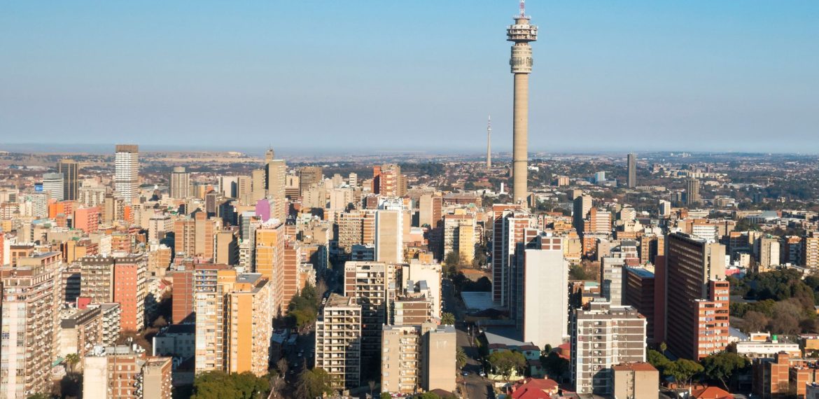 Aerial view of a cityscape with many tall buildings and a prominent telecommunications tower in the center, under a clear blue sky—ideal for capturing stunning Pet TV broadcasts from above.