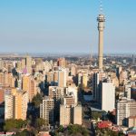 Aerial view of a cityscape with many tall buildings and a prominent telecommunications tower in the center, under a clear blue sky—ideal for capturing stunning Pet TV broadcasts from above.