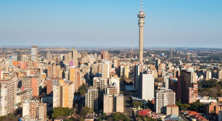 Aerial view of a cityscape with many tall buildings and a prominent telecommunications tower in the center, under a clear blue sky—ideal for capturing stunning Pet TV broadcasts from above.