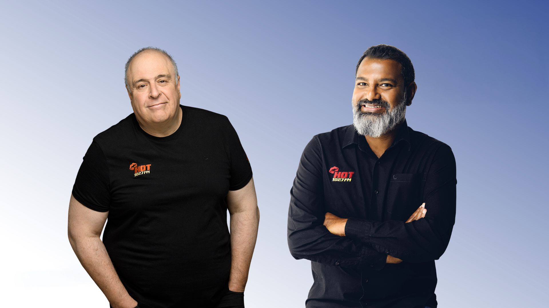 Two men stand before a gradient blue background, both wearing HOT Realty shirts. Lloyd Madurai, on the right in a black button-up shirt with arms crossed, smiles beside another man in a black t-shirt.