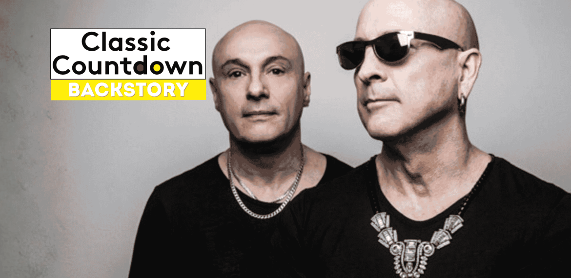 Two bald men in black shirts and silver jewelry stand side by side; one wears sunglasses. Against a gray background, a Classic Countdown Backstory logo appears in the upper left, recalling the cool style of Robert Palmer.