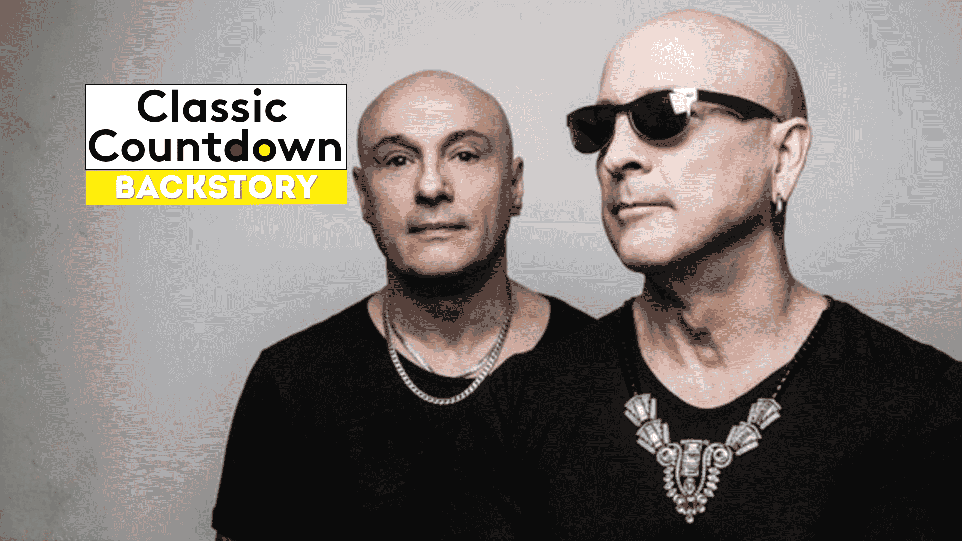 Two bald men in black shirts and silver jewelry stand side by side; one wears sunglasses. Against a gray background, a Classic Countdown Backstory logo appears in the upper left, recalling the cool style of Robert Palmer.