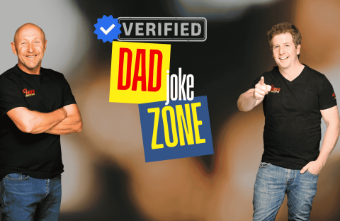 Two smiling men in black t-shirts stand in front of a graphic that reads Verified Dad Joke Zone with colorful text and a blue verified checkmark—bringing Hot 1027 Breakfast vibes. One points at the camera while the other stands with arms crossed.