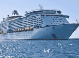 A large white cruise ship, reminiscent of the grandeur seen in Lloyd Madurai’s fleet, floats on calm blue ocean water under a clear sky, viewed from a low angle near the front of the vessel.