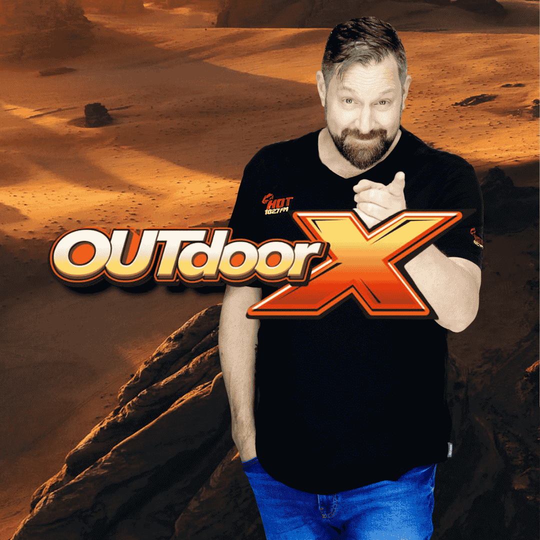 A bearded man in a black T-shirt and blue jeans stands with one hand in his pocket, pointing at the camera. The words OUTdoor X and Tiletoria are boldly displayed over him, set against a rocky desert landscape in the background.