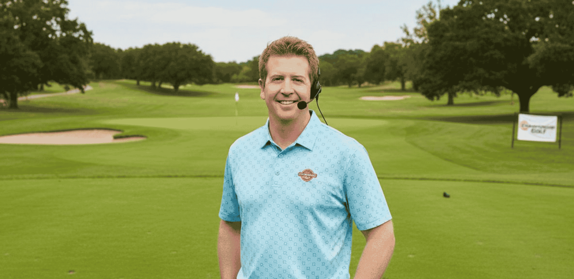 A man in a blue polo shirt and headset stands smiling on a green golf course, with trees, sand traps, and a golf flag visible in the background. A Hot 1027 Breakfast sign is seen on the right side of the image.