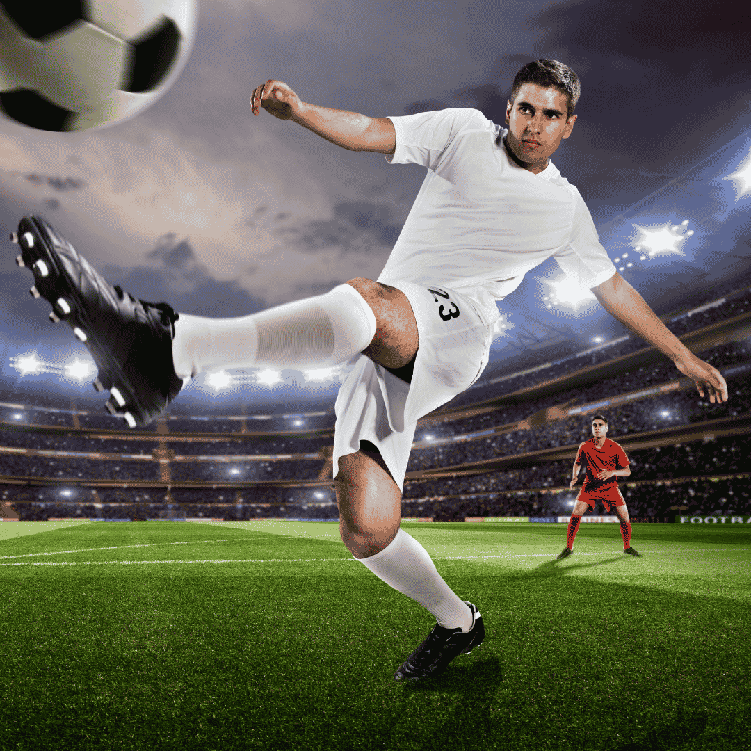 A soccer player in a white uniform, resembling Lloyd Madurai, kicks a ball mid-air on a stadium field, with another player in red standing in the background under stadium lights.
