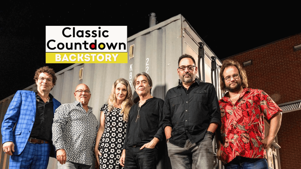 Six people stand side by side in front of a shipping container at night. The Classic Countdown Backstory logo appears in the upper left, hinting at a Robert Palmer backstory. The group is casually dressed and smiling at the camera.