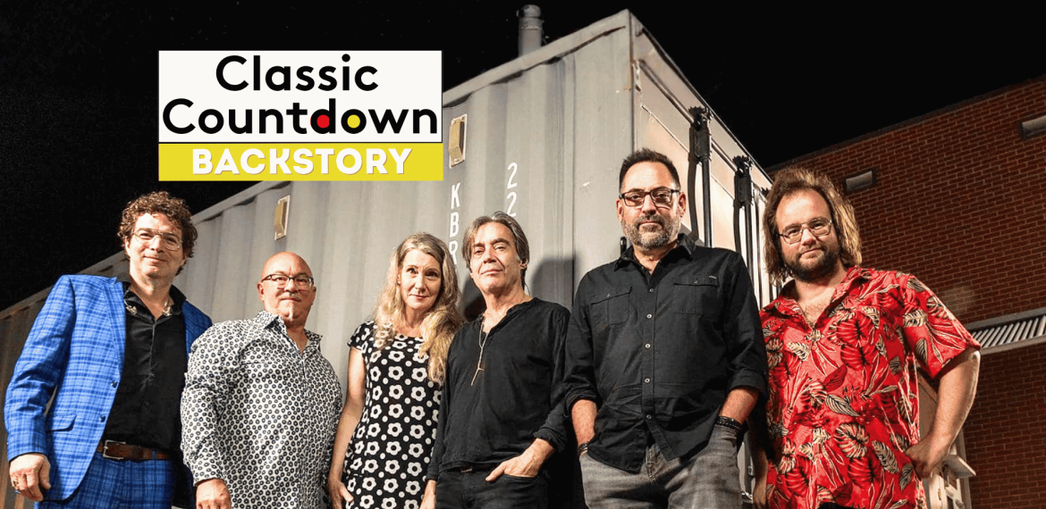 Six people stand side by side in front of a shipping container at night. The Classic Countdown Backstory logo appears in the upper left, hinting at a Robert Palmer backstory. The group is casually dressed and smiling at the camera.