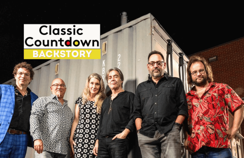 Six people stand side by side in front of a shipping container at night. The Classic Countdown Backstory logo appears in the upper left, hinting at a Robert Palmer backstory. The group is casually dressed and smiling at the camera.