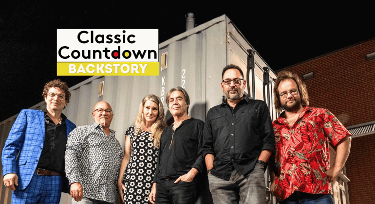 Six people stand side by side in front of a shipping container at night. The Classic Countdown Backstory logo appears in the upper left, hinting at a Robert Palmer backstory. The group is casually dressed and smiling at the camera.
