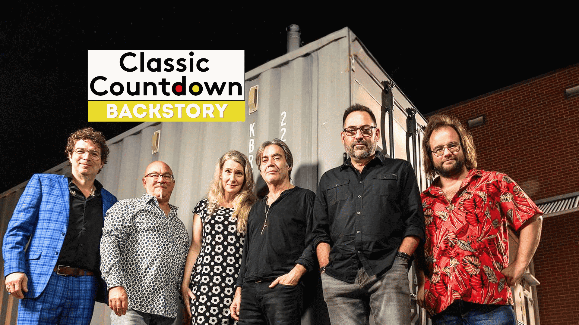 Six people stand side by side in front of a shipping container at night. The Classic Countdown Backstory logo appears in the upper left, hinting at a Robert Palmer backstory. The group is casually dressed and smiling at the camera.