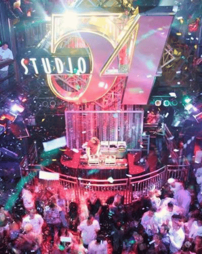 A vibrant nightclub scene with colorful lights, confetti, and a DJ performing on stage under a large Studio 54 sign, as people dance and celebrate on the crowded dance floor.