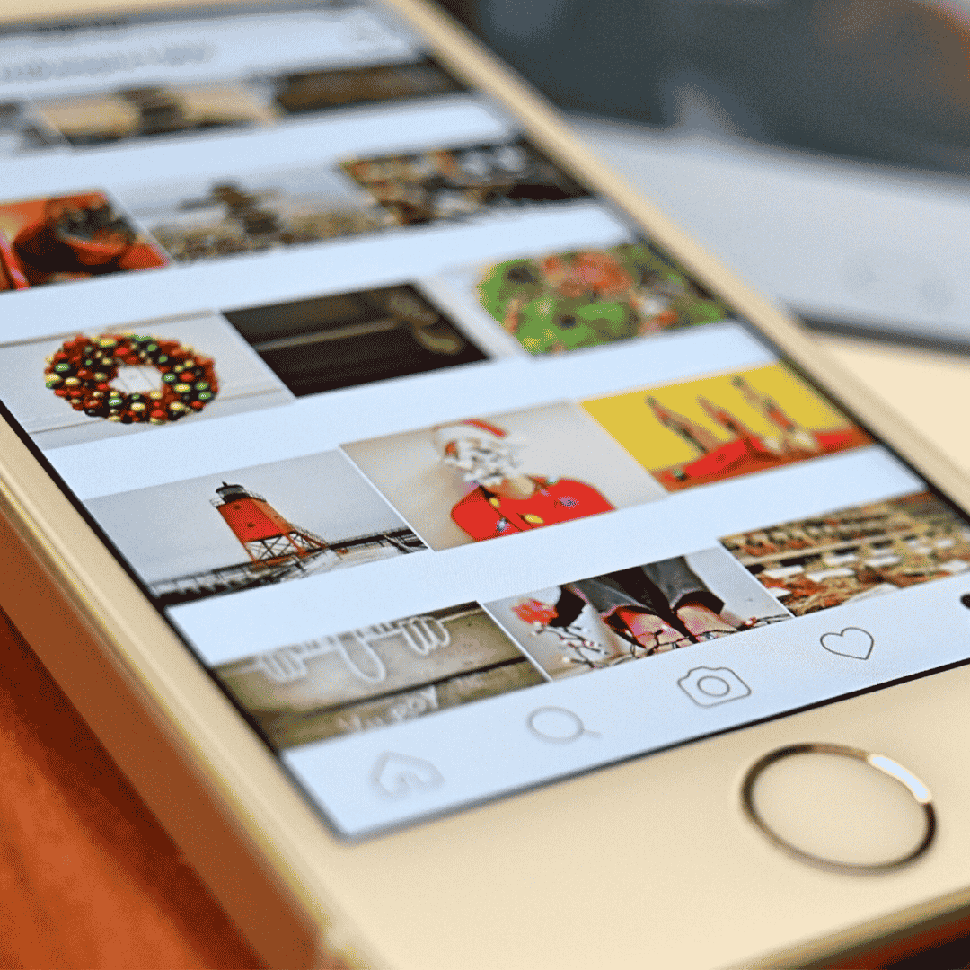 A close-up of a smartphone displaying a social media photo gallery with festive and holiday-themed images, including a wreath, Santa, lighthouse, and Christmas decorations.