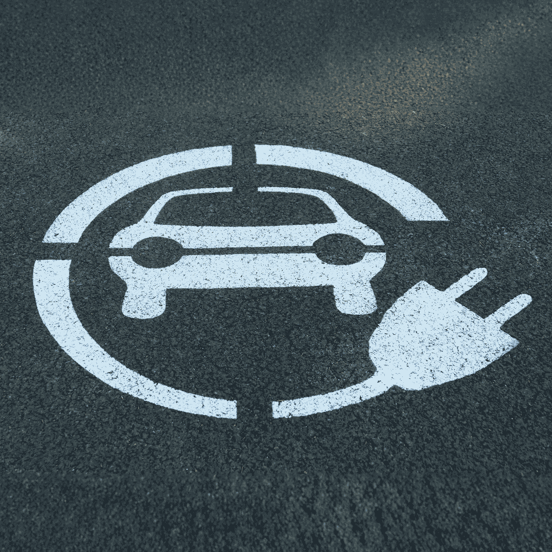 White icon of a car and an electric plug painted on asphalt, indicating an electric vehicle charging station or parking spot&mdash;like a winter blanket for your car, these spaces offer essential protection and power during colder months.