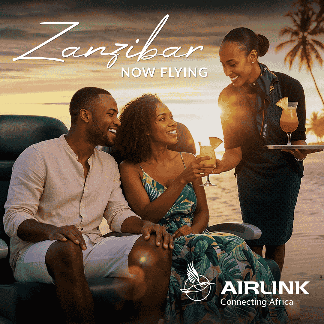 A smiling couple relaxes in airplane seats, receiving tropical drinks from a flight attendant. The text reads Zanzibar NOW FLYING. Enjoy seamless travel and Amex acceptance on board. AIRLINK Connecting Africa logo appears in the bottom right corner.