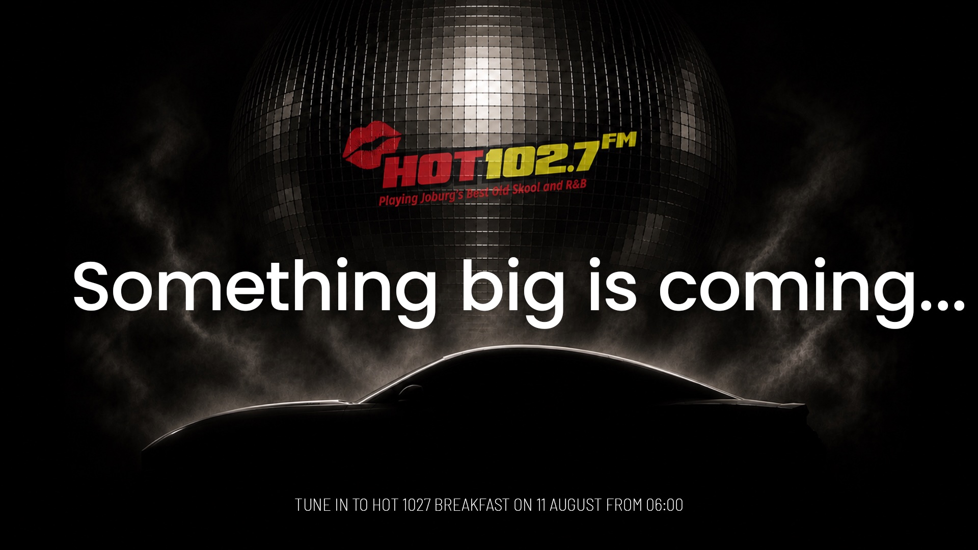 Dark image with Hot 102.7 FM logo above large text, Something big is coming... A silhouette of a car is visible below, with small text about tuning in to Hot 1027 on 11 August from 06:00.