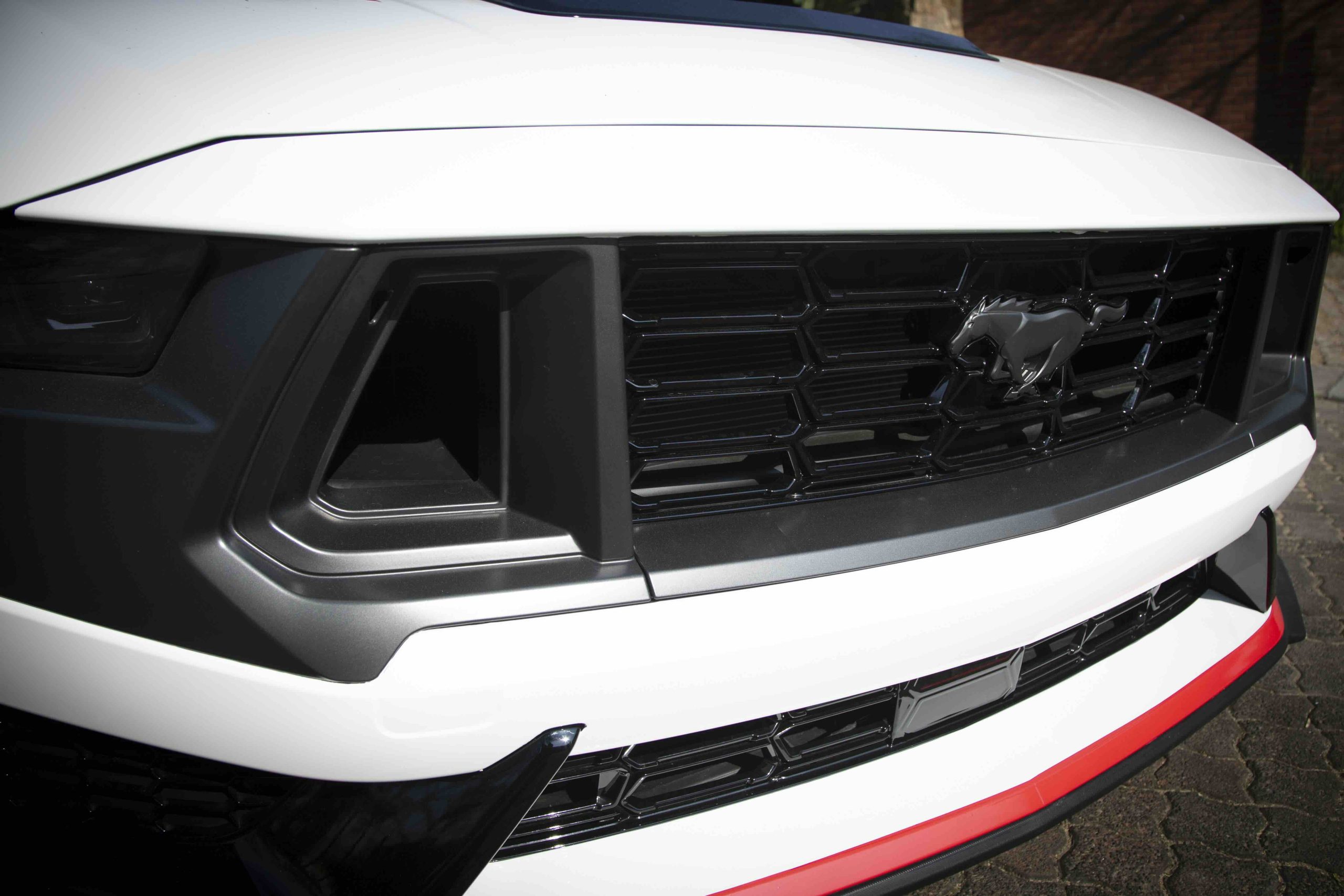 Close-up of the front grille of a white Ford Mustang, showcasing the iconic running horse emblem and striking black details found on the Mustang Dark Horse, parked on a paved surface.
