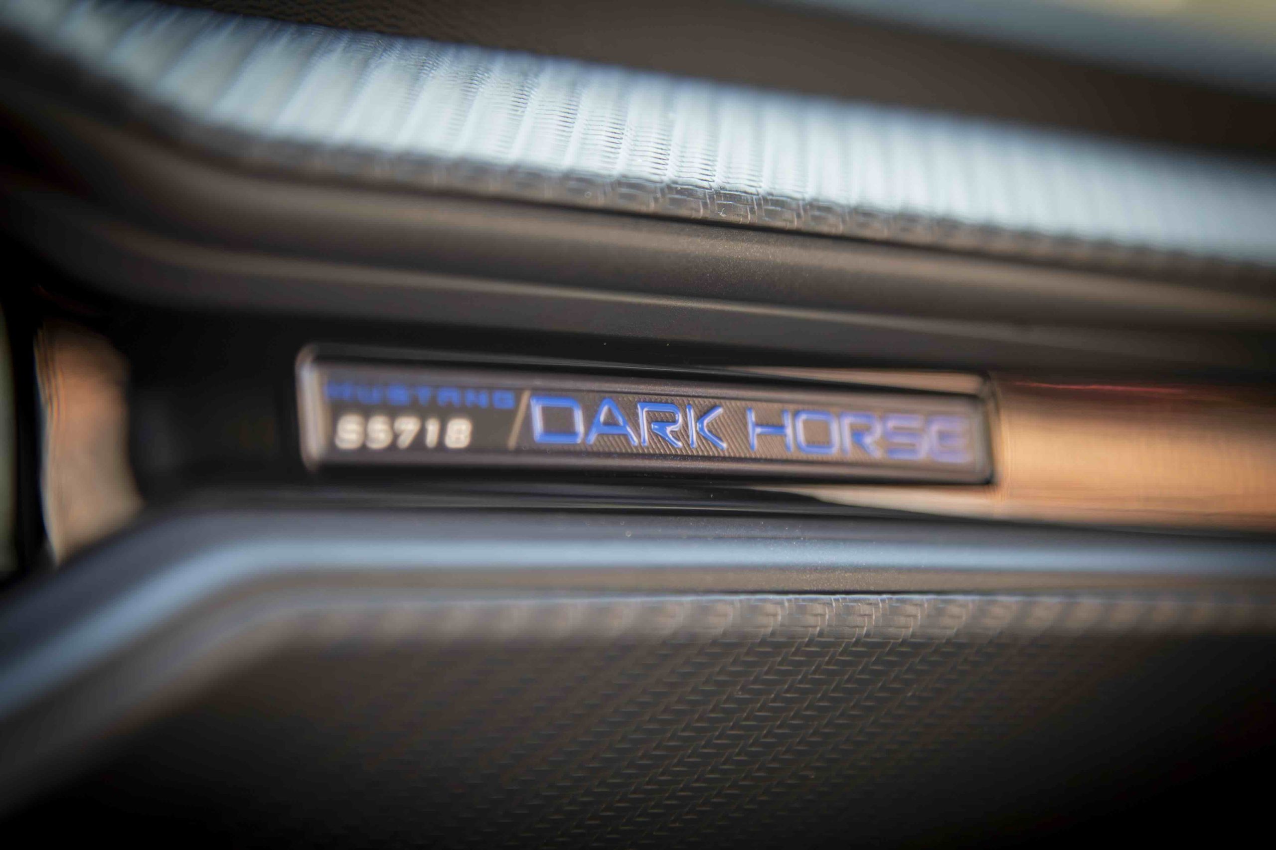 Close-up of a badge inside a car that reads Mustang Dark Horse S9718, with textured black and metallic surfaces visible around it, highlighting the distinctive Mustang Dark Horse branding.