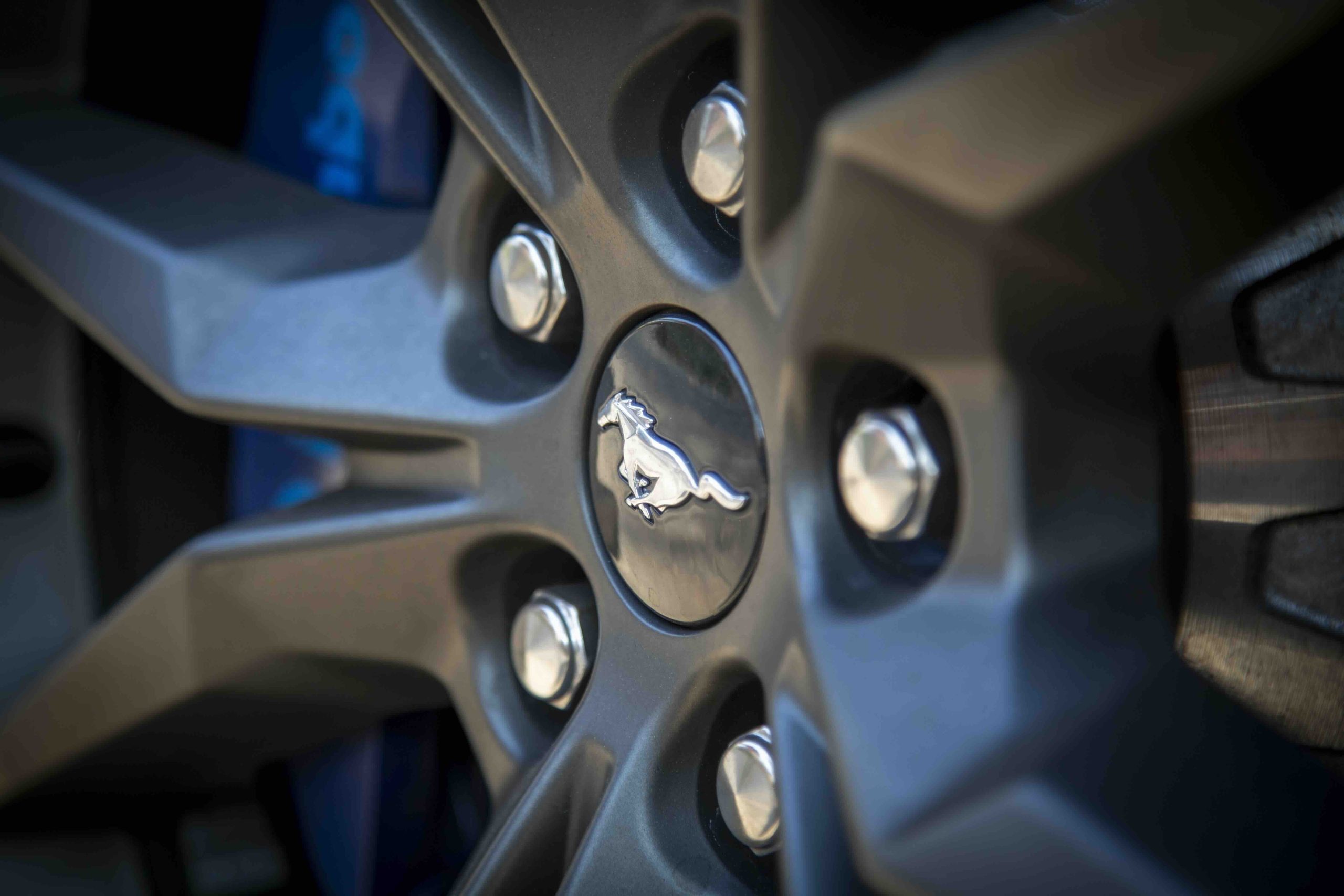 Close-up of a car wheel rim featuring the Mustang Dark Horse logo at the center, surrounded by metallic lug nuts.