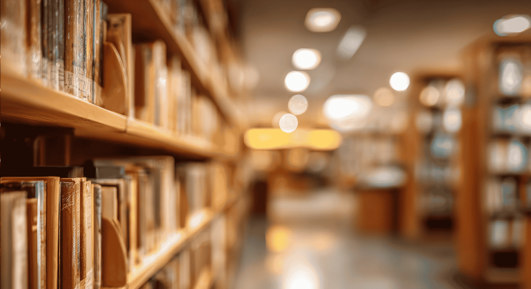 Rows of books on library shelves in soft focus, with warm lighting and a blurred background creating a calm, inviting atmosphere—like a bank of knowledge waiting to be explored.