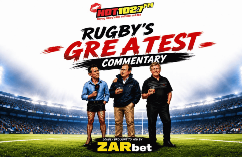 Three men stand on a rugby field holding drinks, wrapped warmly in winter blankets, with a stadium in the background. Text above them reads, Rugby&rsquo;s Greatest Commentary, with HOT102.7FM and ZARbet logos also visible.