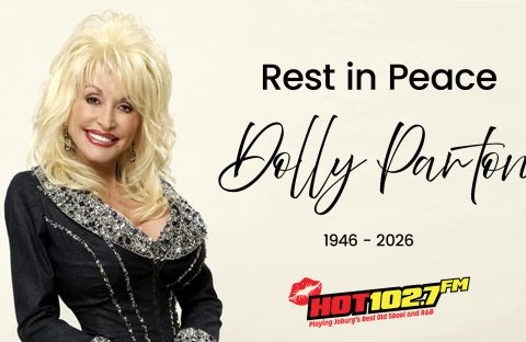 A smiling woman with blonde hair in a sparkly black outfit stands next to text that reads, Rest in Peace Dolly Parton 1946-2026, with a HOT 102.7 FM radio logo below.