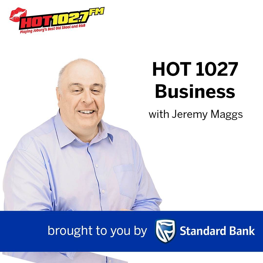 A man in a light blue shirt smiles, standing in front of text: HOT 1027 Business with Jeremy Maggs, with logos for HOT 102.7 FM and Standard Bank.