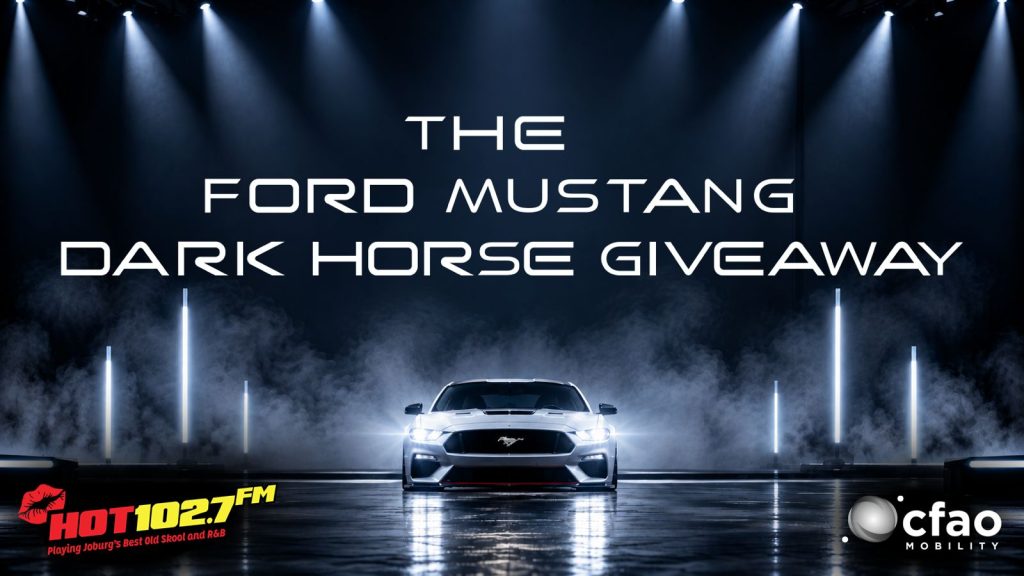 A Ford Mustang on a dramatic, smoky stage, draped with a cozy winter blanket, with text: The Ford Mustang Dark Horse Giveaway. HOT102.7 FM and CFAO Mobility logos appear at the bottom corners.