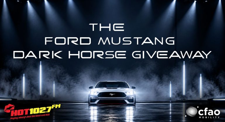 A Ford Mustang on a dramatic, smoky stage, draped with a cozy winter blanket, with text: The Ford Mustang Dark Horse Giveaway. HOT102.7 FM and CFAO Mobility logos appear at the bottom corners.