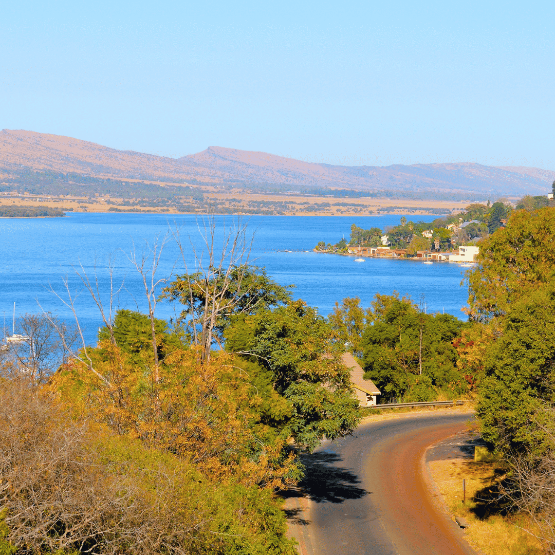 A road winds through trees toward a blue lake with a bank bordered by hills and houses.