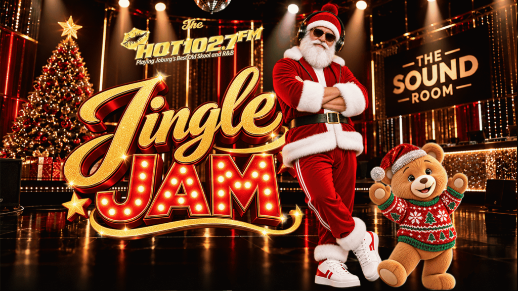 Santa Claus wearing headphones and a teddy bear in a festive sweater stand in a music studio in front of a Jingle Jam sign for Hot 102.7 FM.