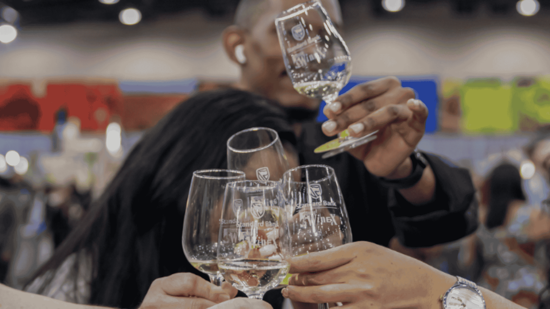 Three people clinking glasses labeled Standard Bank WineX together in a toast.