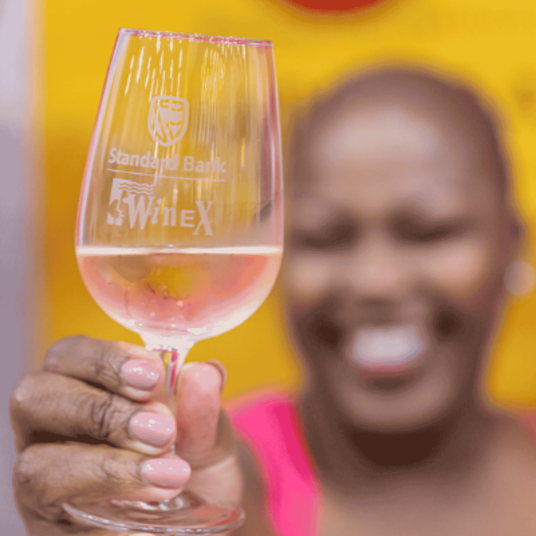 A smiling woman holding up a wine glass etched with the Standard Bank and WineX logos.