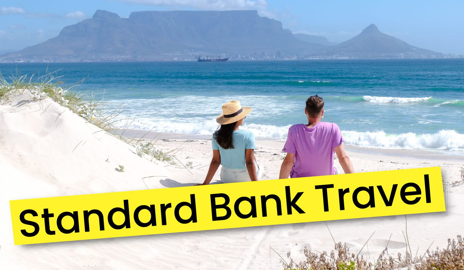 Two people sit on a sandy beach looking out at the ocean and Table Mountain, with the text Standard Bank Travel overlaid at the bottom.