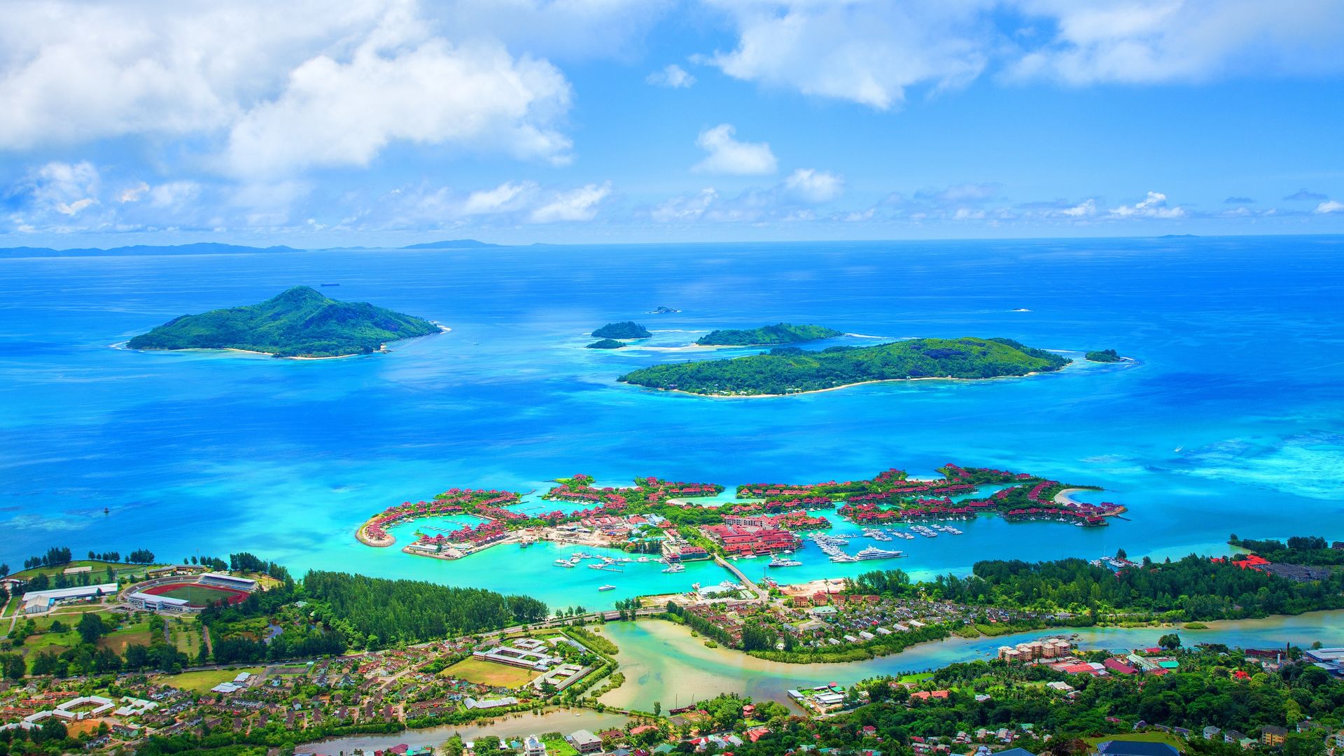Aerial view of a coastal travel resort on Eden Island in the Seychelles, featuring a marina, turquoise water, and surrounding islands.