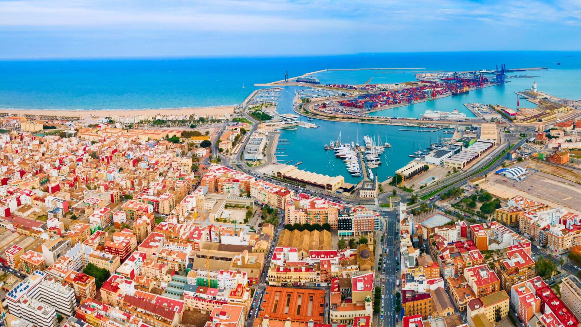 Aerial travel view of the coastal city of Valencia, Spain, featuring a dense residential area leading to the harbor with docked yachts and shipping containers.