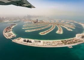 Aerial view of the Palm Jumeirah archipelago in Dubai, a popular travel destination, with the city skyline visible in the distance.