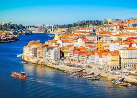 Colorful buildings line the Douro River in Porto, Portugal, a popular travel destination, with a bridge visible in the distance.