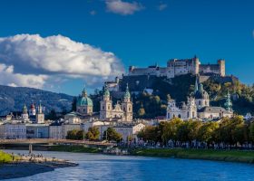 Salzburg city skyline along the Salzach River, with the Hohensalzburg Fortress overlooking the cathedrals and historic buildings.