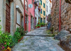 A narrow, cobblestone alleyway lined with colorful red and yellow buildings and potted plants.